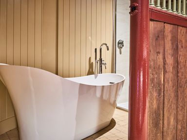 A bathroom with a white freestanding bathtub and a red wooden partition at The Stallion in Humshaugh