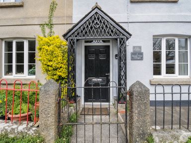 The front entrance of a cottage with a black wooden door and a black metal porch covering at Hobbs Cottage in Sticklepath