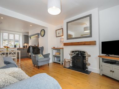A living room with a fireplace armchair and television next to an open kitchen at Hobbs Cottage in Sticklepath