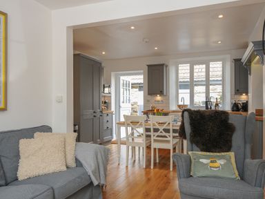 A living room with a gray sofa and armchair next to a dining table and kitchen with gray cabinets at Hobbs Cottage in Sticklepath