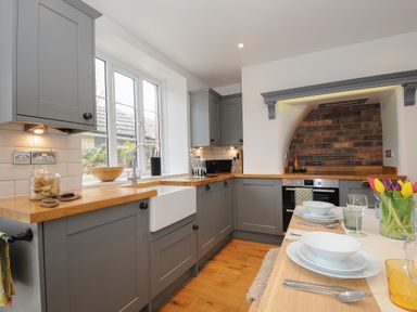 A kitchen with grey cabinets wooden countertops a white sink and a dining table with white dishes and tulips at Hobbs Cottage in Sticklepath
