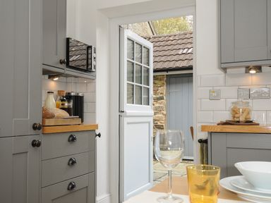 A kitchen with grey cabinets a wooden countertop a microwave open door leading outside at Hobbs Cottage in Sticklepath