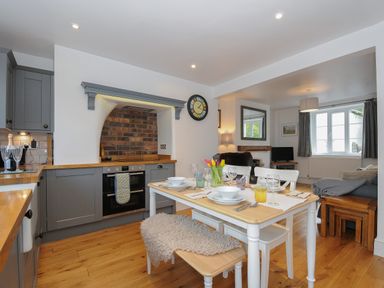 A kitchen and dining area with a wooden table set for four and a living room with a sofa and TV at Hobbs Cottage in Sticklepath