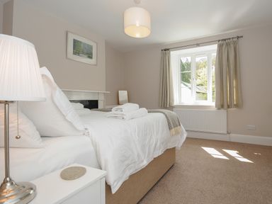 A bedroom with a double bed bedside table lamp window with curtains and a landscape painting on the wall at Hobbs Cottage in Sticklepath