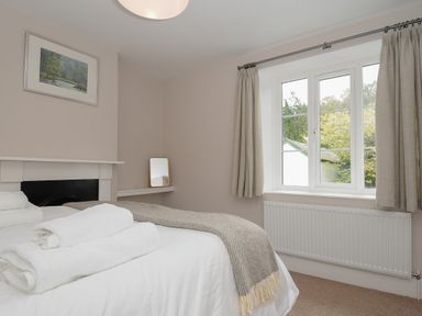 A bedroom with a bed with white linens and towels a window with curtains a radiator a painting and a small mirror at Hobbs Cottage in Sticklepath