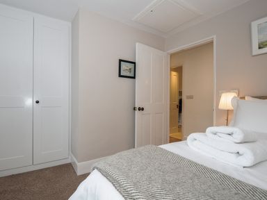 A bedroom with a bed folded towels bedside lamp and an open door at Hobbs Cottage in Sticklepath