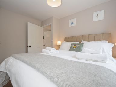 A bedroom with a bed made with white linens and grey blanket with a lamp on each side at Hobbs Cottage in Sticklepath