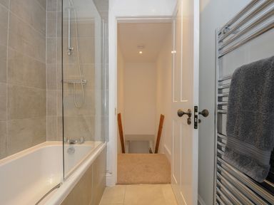 A bathroom with a bathtub and shower and a towel rack with towels at Hobbs Cottage in Sticklepath