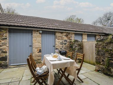 An outdoor patio area with a dining table set with tea cups and plates surrounded by wooden chairs at Hobbs Cottage in Sticklepath