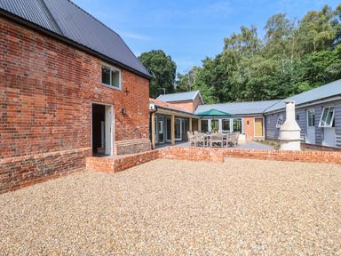 An outdoor patio area with brick buildings gravel ground and wooden table with chairs and umbrella at Church Farm Barn Dunwich near Westleton