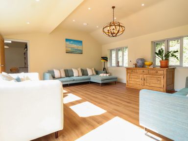 A living room with blue sofas a wooden sideboard and a chandelier at Church Farm Barn in Dunwich near Westleton