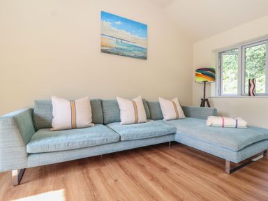 A living room with a light blue sectional sofa with cushions a colorful floor lamp and a painting on the wall at Church Farm Barn in Dunwich near Westleton