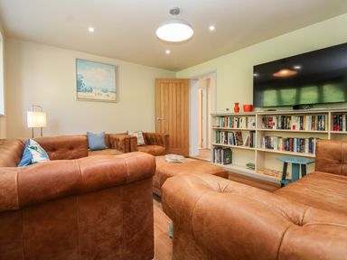 A living room with brown leather sofas a bookshelf a flat screen television a lamp and a painting at Church Farm Barn Dunwich near Westleton