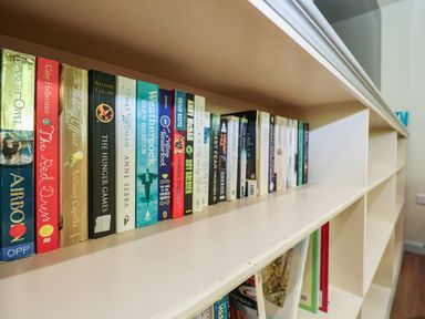 A white bookshelf with various books arranged on top and some books and folders inside the shelves at Church Farm Barn in Dunwich near Westleton