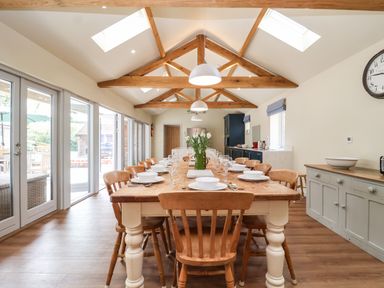 A dining room with a long wooden table set with dishes and glasses under wooden ceiling beams at Church Farm Barn in Dunwich near Westleton