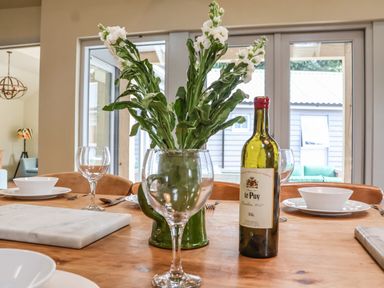 A dining table with a green vase of flowers a bottle of wine wine glasses and plates at Church Farm Barn Dunwich near Westleton