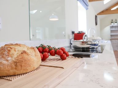 A kitchen countertop with bread, cherry tomatoes on a cutting board, a knife, and a pot on the stove at Church Farm Barn in Dunwich near Westleton