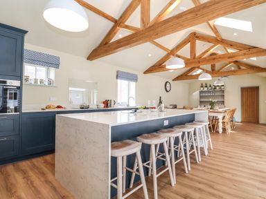 A kitchen with a large island and bar stools under exposed wooden beams at Church Farm Barn in Dunwich near Westleton