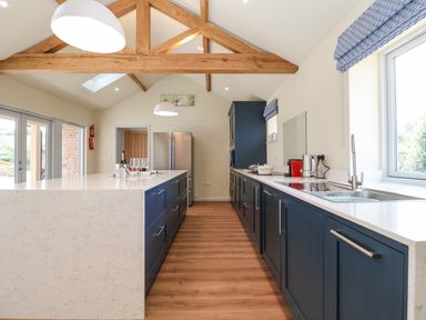 A kitchen with blue cabinets a white island wooden beams and large windows at Church Farm Barn Dunwich near Westleton