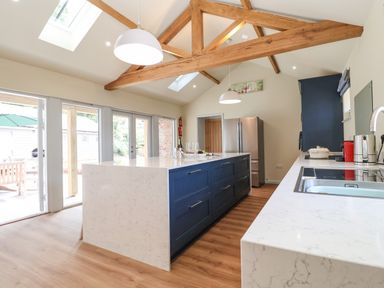A kitchen with a large island with blue cabinets a stainless steel refrigerator and wooden ceiling beams at Church Farm Barn Dunwich near Westleton