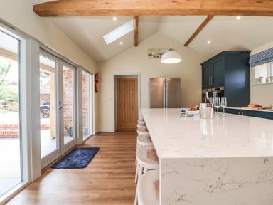 A kitchen with a large marble island and stools next to glass doors at Church Farm Barn Dunwich near Westleton