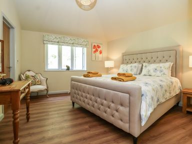 A bedroom with a large bed with floral bedding and yellow towels on top a wooden desk and an armchair near a window at Church Farm Barn Dunwich near Westleton