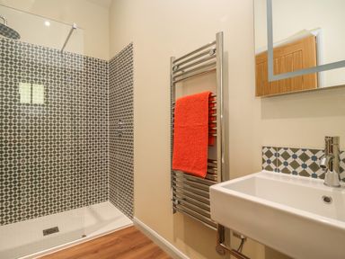 A bathroom with a walk in shower with tiled walls a metal towel rack with a red towel and a sink at Church Farm Barn in Dunwich near Westleton