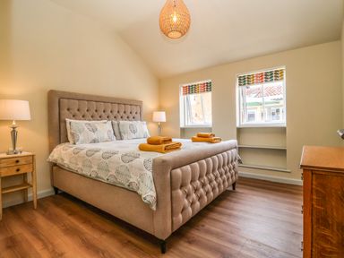 A bedroom with a beige bed and leaf patterned bedding with two windows at Church Farm Barn Dunwich near Westleton