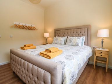 A bedroom with a double bed with patterned bedding and folded towels on it two bedside tables with lamps and a wall rack with hangers at Church Farm Barn Dunwich near Westleton