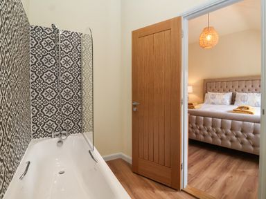A bathroom with a bathtub and patterned tiles next to a bedroom with a bed and a pendant light at Church Farm Barn Dunwich near Westleton