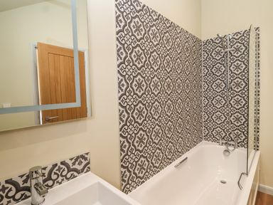 A bathroom with a white bathtub shower tap and patterned tiled wall at Church Farm Barn Dunwich near Westleton