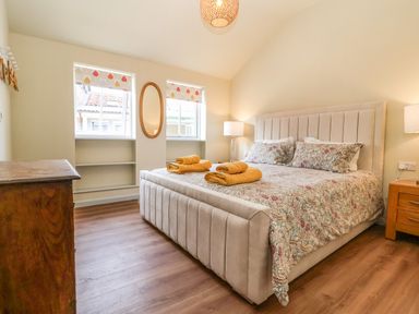 A bedroom with a large bed with patterned bedding and yellow towels beside windows and wooden furniture at Church Farm Barn Dunwich near Westleton