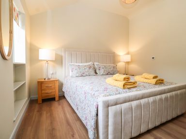 A bedroom with a bed with patterned bedding and yellow towels bedside tables with lamps and a round mirror on the wall at Church Farm Barn Dunwich near Westleton