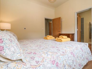 A bedroom with a patterned bedspread and two stacks of yellow towels on the bed a lamp on a side table wooden doors and a chest at Church Farm Barn Dunwich near Westleton