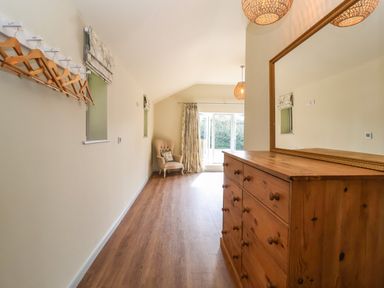 A hallway with wooden floor a wooden dresser with a large mirror an armchair with a cushion and hanging wooden coat hangers at Church Farm Barn Dunwich near Westleton