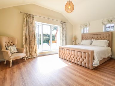 A bedroom with a tufted bed and an armchair next to sliding glass doors at Church Farm Barn in Dunwich near Westleton