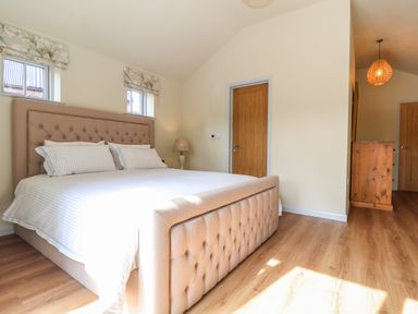 A bedroom with a large bed two windows bedside lamp wooden doors and a wooden chest of drawers at Church Farm Barn Dunwich near Westleton