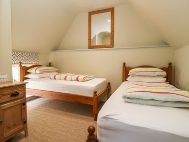 A bedroom with two single beds with striped bedding a wooden nightstand and a mirror on the wall at Church Farm Barn Dunwich near Westleton