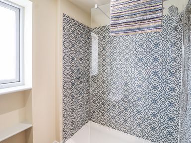 A shower with patterned tile walls a glass panel and a window at Church Farm Barn in Dunwich near Westleton