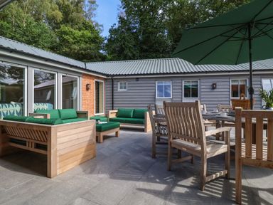 An outdoor patio with wooden chairs and tables with green cushions and umbrellas at Church Farm Barn in Dunwich near Westleton