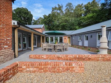 An outdoor patio with a wooden dining table and chairs under a green umbrella at Church Farm Barn Dunwich near Westleton