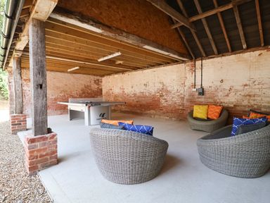 A covered outdoor area with a ping pong table and wicker chairs with colorful cushions at Church Farm Barn Dunwich near Westleton