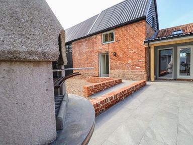 An outdoor patio area with a built in barbecue and brick walls at Church Farm Barn in Dunwich near Westleton