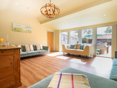 A living room with two sofas a wooden cabinet and large windows showing an outdoor seating area at Church Farm Barn Dunwich near Westleton