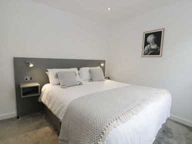 A bedroom with a double bed white and grey bedding wall-mounted reading lights and a framed artwork on the wall at Classic Lodge 16 in Dyserth