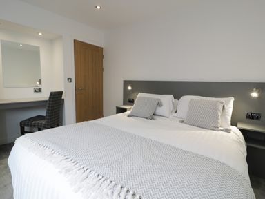 A bedroom with a double bed two pillows a gray headboard wooden door and a desk with a chair at Classic Lodge 16 in Dyserth