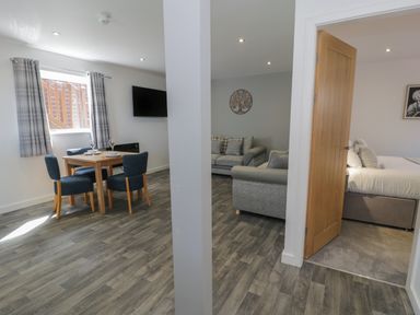 A dining area with table and chairs next to a living area with sofas and an open door leading to a bedroom at Classic Lodge 16 in Dyserth
