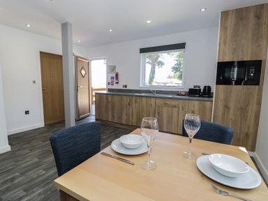 A kitchen and dining area with wooden cabinets a window and a table set with plates bowls wine glasses and cutlery at Classic Lodge 16 in Dyserth