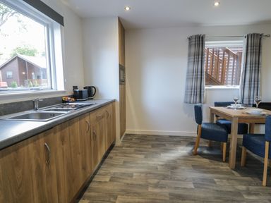 A kitchen with wooden cabinets and a dining table with four blue chairs at Classic Lodge 16 in Dyserth