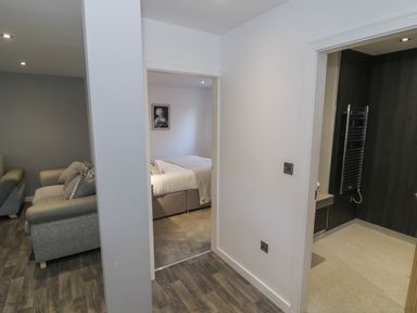 View of a hallway with doorways leading to a living room with sofas a bedroom with a bed and a bathroom with a towel rack at Classic Lodge 16 in Dyserth